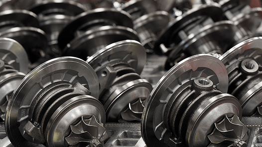 Zbliżenie na wiele nowo wyprodukowanych rdzeni turbosprężarek samochodowych, ułożonych w rzędach w zakładzie produkcyjnym.