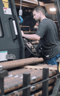 Pracownik obsługujący maszynę przemysłową, skupiony na ustawieniach urządzenia w hali produkcyjnej