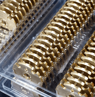 Zbliżenie na rzędy nowo wyprodukowanych, precyzyjnie obrobionych mosiężnych kół zębatych, starannie ułożonych w przezroczystych plastikowych tackach opakowaniowych.