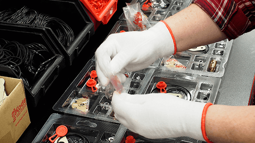 Pracownik fabryki w białych rękawiczkach starannie kompletuje zestaw naprawczy do turbosprężarki, umieszczając małe komponenty w podzielonej plastikowej tacy.