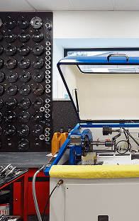 Szybkobieżna wyważarka do komponentów turbosprężarek w profesjonalnym warsztacie, z uporządkowaną ścianą z adapterami do kalibracji w tle.