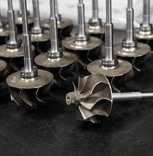 Zbliżenie na liczne, precyzyjnie wykonane wałki turbinowe turbosprężarek z zamontowanymi kołami kompresji, gotowe do kolejnego etapu montażu.